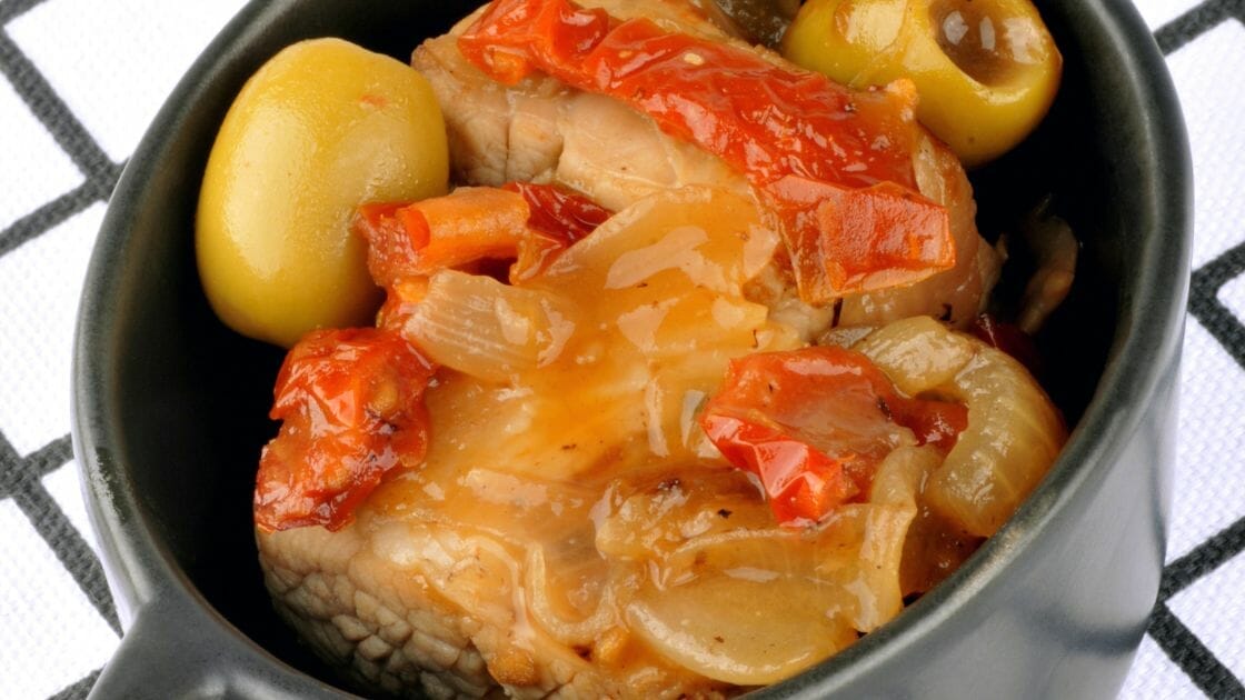 Un bol de viande cuite avec des poivrons rouges tranchés, des oignons et des olives vertes.