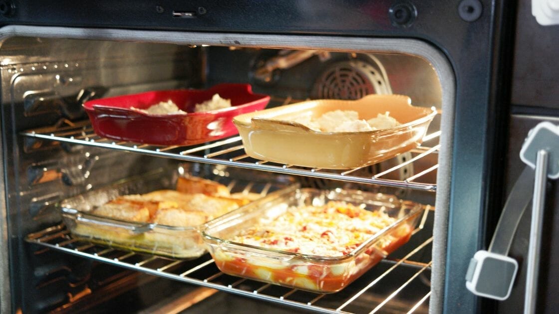 Deux grilles de four avec quatre plats à gratin. La grille supérieure est équipée de plats rouges et beiges, tandis que la grille inférieure est équipée de deux plats en verre. On y voit divers produits de boulangerie et des plats à gratin.