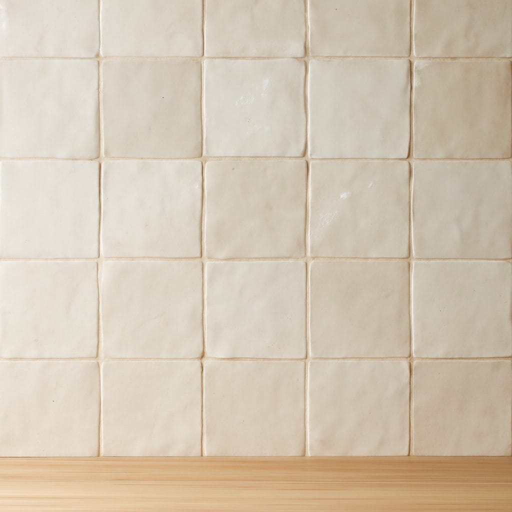 Carreaux carrés de couleur crème sur un mur au-dessus d'une surface en bois clair, disposés en grille.